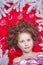 A small fair-haired girl lying on a red floor with a Christmas garland and fir branches around her head