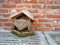 Small fallen wooden birdhouse with snow against the side of a red brick house