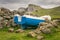 A small fishing boat moored on land nect to a stone wall. kilt rock in the backgrond