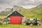 A small fishing boat moored on land next to a stone wall. kilt rock in the backgrond. a red door stone built hut