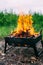 A small folding portable brazier filled with burning wood. Cooking on the grill. Safe fire in nature