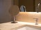 Small folding round makeup mirror standing near sink basin with marble top and steel faucet.