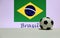 Small football on the white floor and Brazilian nation flag with the text of Brazil background.