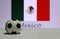 Small football on the white floor and Mexican nation flag with the text of Mexico background.