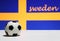 Small football on the white floor and out focus Swedish nation flag with the text of Sweden background.
