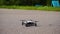 Small four-propeller drone takes off from the asphalt.