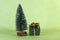 Small gift placed next to a Christmas tree decorative and miniature on green background