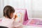 Small girl artist with pigtails posing backwards to camera and painting, child drawing house, uses colored pencils and wax crayons