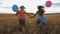 Small girl and boy holding hands of each other and running among barley plantation. Couple of little kids with balloons