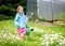 Small girl child is gardening and watering daisies in backyard.