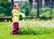 Small girl child is gardening and watering daisies in backyard.