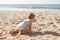 Small girl crawls on sand at beach near the sea