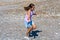 Small girl in pastel clothes running along the riverbank with a reed in hand