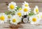 Small glass bottle with essential chamomile oil on the old wooden background. Chamomile flowers, close up.