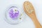 Small glass bowl with purple bath salts foot soak, wooden hairbrush and white flowers. Top view