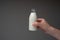 Small glass milk bottle with cap held in hand by Caucasian male. Close up studio shot,  on gray background