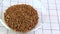 small grains of brown buckwheat in a transparent plate on a white background, the video image moves from right to left