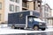 Small gray freight truck parked against the facade of a residential building