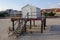 A small gray shack a platform raised above the sand on wooden pilings at a beach