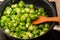 Small green cabbages of Brussels sprouts are stirred with a spatula in a frying pan. Kitchen top plate and stove on the