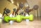 Small green dumbbells on the wooden floor. Fitness gears in the gym with girls doing exercises with balls on the background. Sport