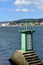 Small green lighthouse in a bay. Small coastal village, blue water. Sunny day, blue sky with clouds. Galicia, Spain.