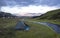 Small green tent standing on green grass on creek banks campsite Strutur near road f210, snow patched hills, midnight