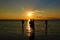 Small group of silhouetted young people wade in shallow waters and watch the sunset.