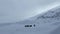 Small group of tourists with backpacks and trekking poles are walking along a snow-covered trail in the mountains.