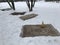 Small handmade Persian rugs lie on the snow for cleaning, one on top of a broom.