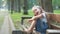 Small happy child girl sitting on a bench resting in summer park.