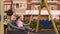 Small happy children ride on a round swing with ropes in the courtyard.