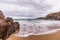 Small hidden beach between rocks, cliffs and islands in the distance, moody stormy clouds