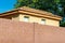 Small house or building with white stucco exterior and adobe orange roof with brown brick fence or wall foreground