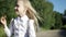 A small hungry blonde school girl goes to school on the sandy road through the field and eats a biscuit.