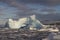 small iceberg in Antarctic waters clogged with ice against a rocky shore