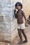 Small indian barefoot boy in worn out poor clothes playing with the wall in the street