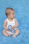 A small infant sits on a blue background with a toy