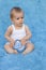 A small infant sits on a blue background with a toy