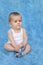 A small infant sits on a blue background with a toy