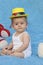 A small infant sits on a blue background with a toy