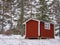 A small, intensely red storage building on a farm. There are no windows and the door is closed. Building is very old but kept fine