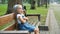 Small irritated child girl sitting alone on a bench in summer park