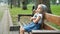 Small irritated child girl sitting alone on a bench in summer park