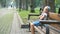 Small irritated child girl sitting alone on a bench in summer park