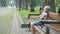 Small irritated child girl sitting alone on a bench in summer park.