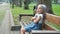 Small irritated child girl sitting alone on a bench in summer park