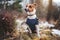 Small Jack Russell terrier sitting on snow covered forest path wearing warm jumper