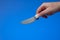 Small kitchen buttering spending knife with white plastic handle held by male hand. Close up studio shot, isolated on blue