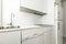 Small kitchen furnished with white furniture, white integrated appliances, stone countertop of the same color and veined marble